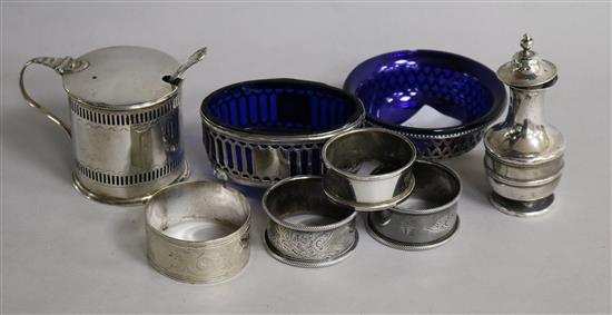 Four silver condiments including damaged George III mustard and a sterling silver salt and four napkins rings (3x silver).